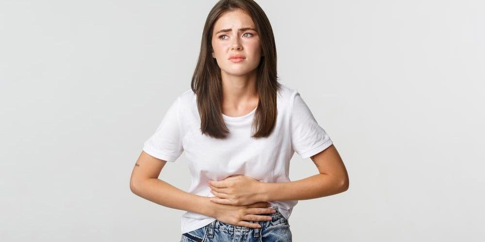 Young woman bending forward, holding her stomach in pain.