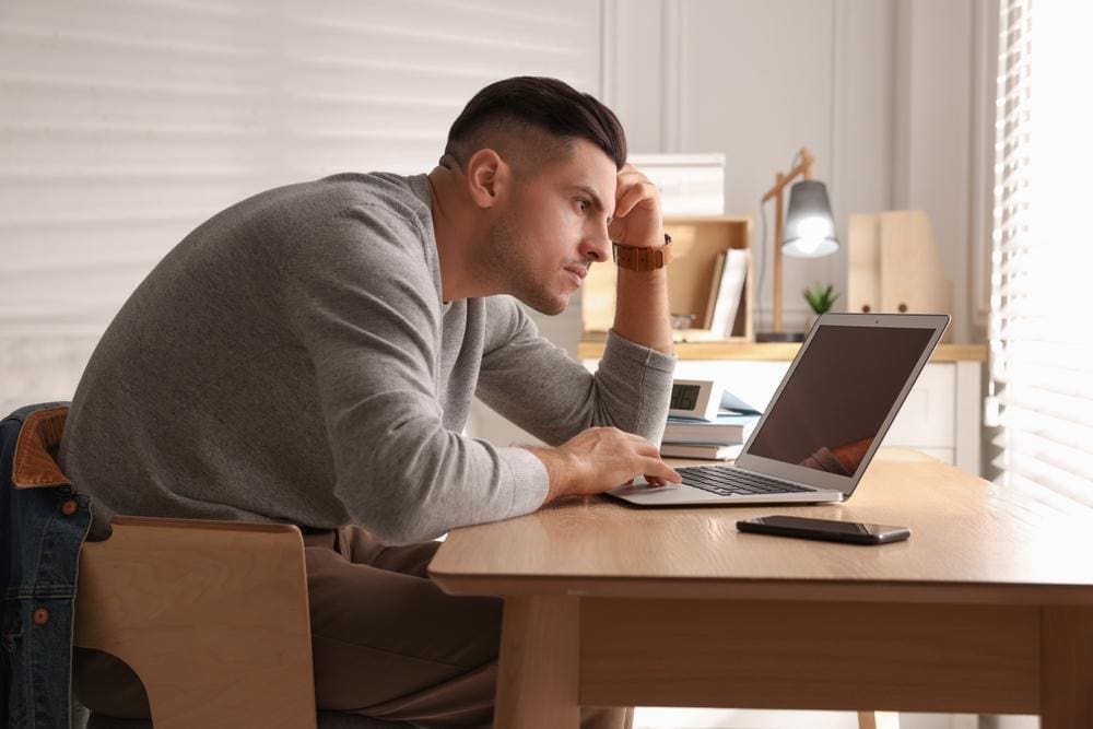 Man sits at a desk hunched over his laptop.