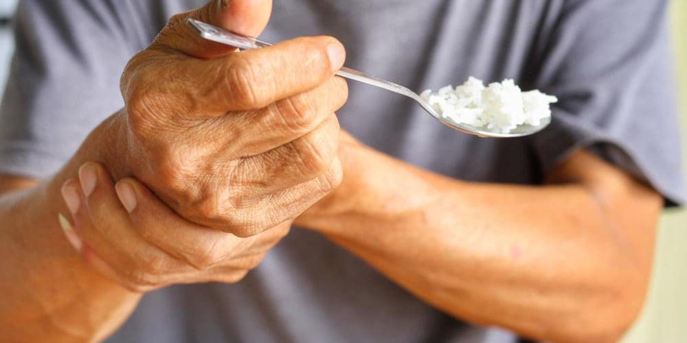 A man with Parkinson's disease holding his wrist while trying to feed himself with a spoon.