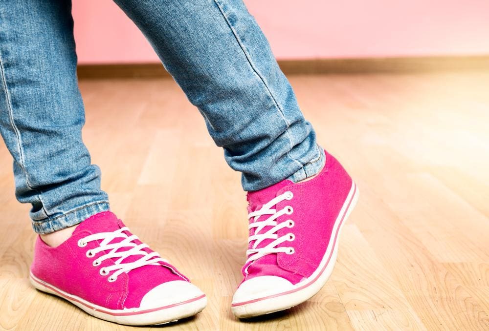 Feet of a girl with pigeon toes wearing bright pink sneakers.