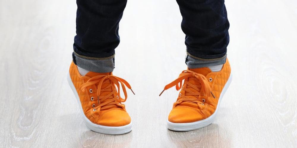 Child with pigeon toes wearing orange sneakers.