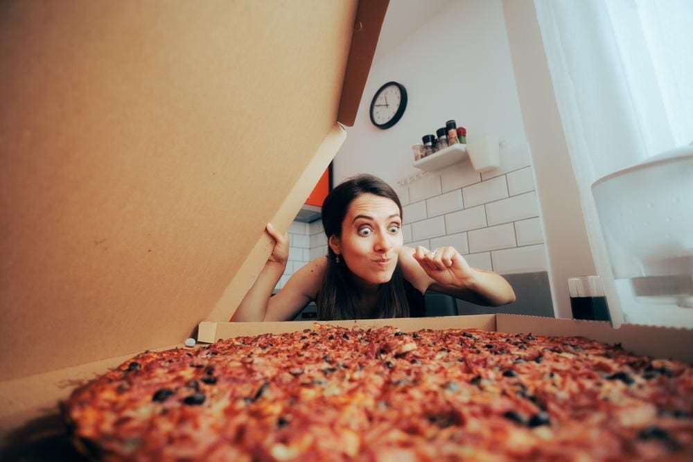 Woman looking excitedly at a pizza.
