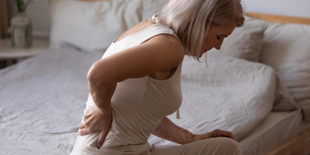Mature woman sitting on the edge of bed with back pain caused by subluxation.