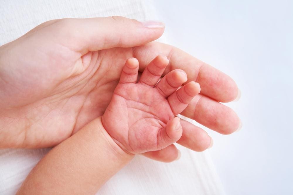 Mother holds her baby's hand.