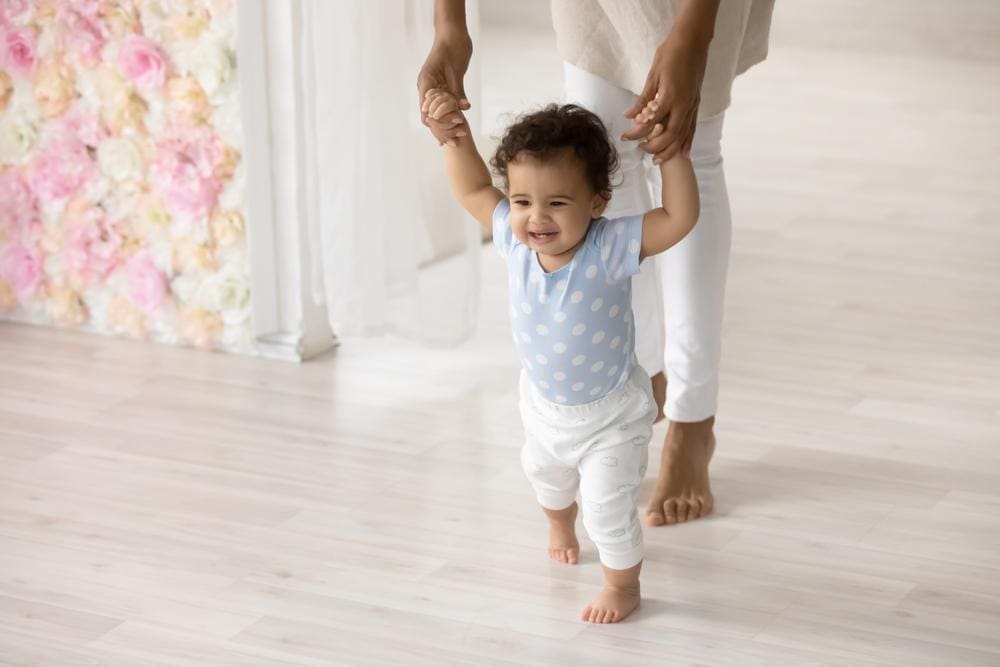 Young toddler learning how to walk with mother holding his hands.