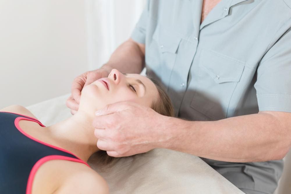 Chiropractor massages a patient's jaw.
