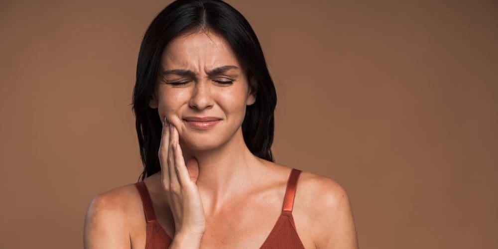 A woman is holding her jaw in pain.