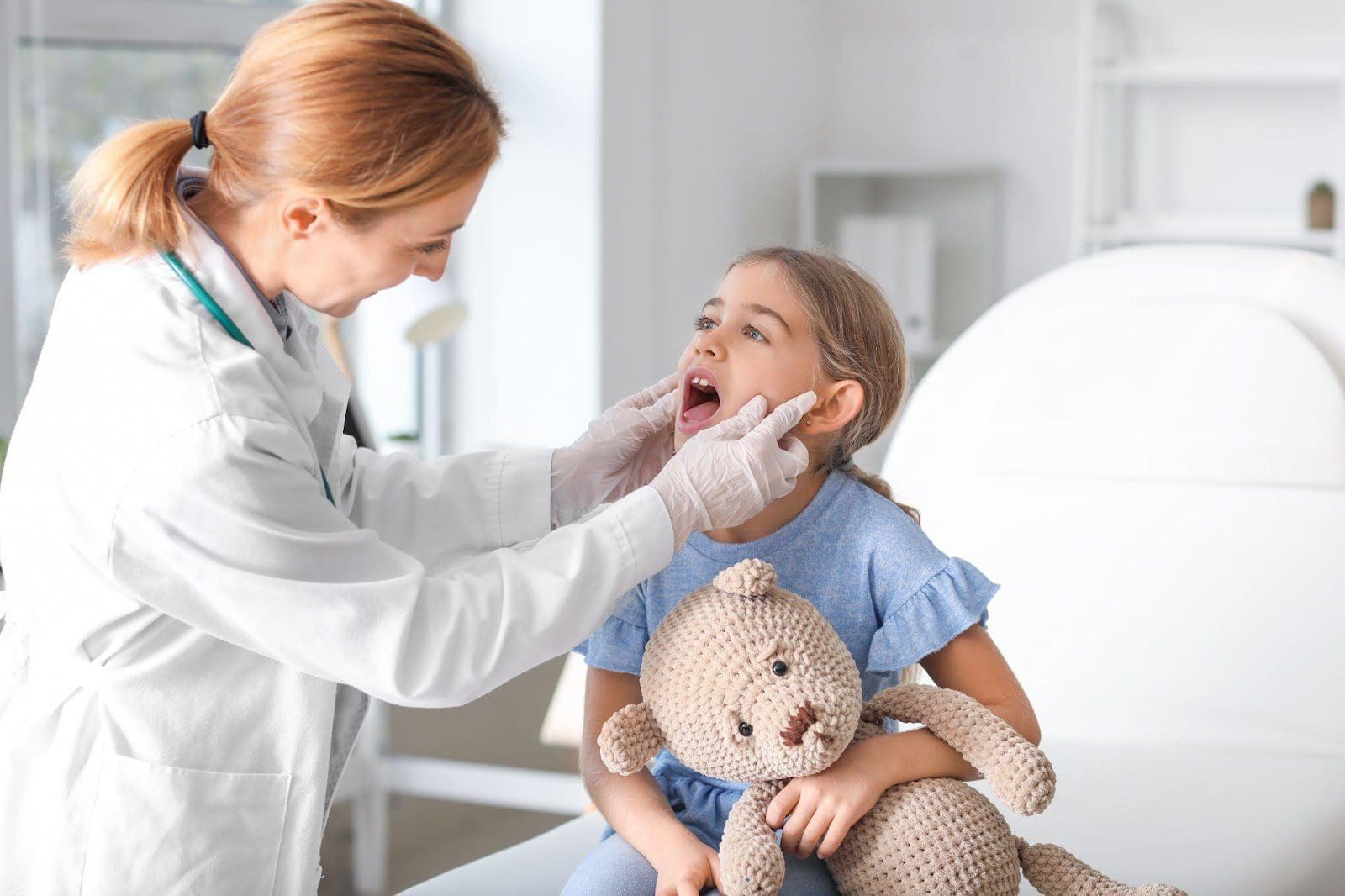 A pediatrician looks into a young girl's throat.
