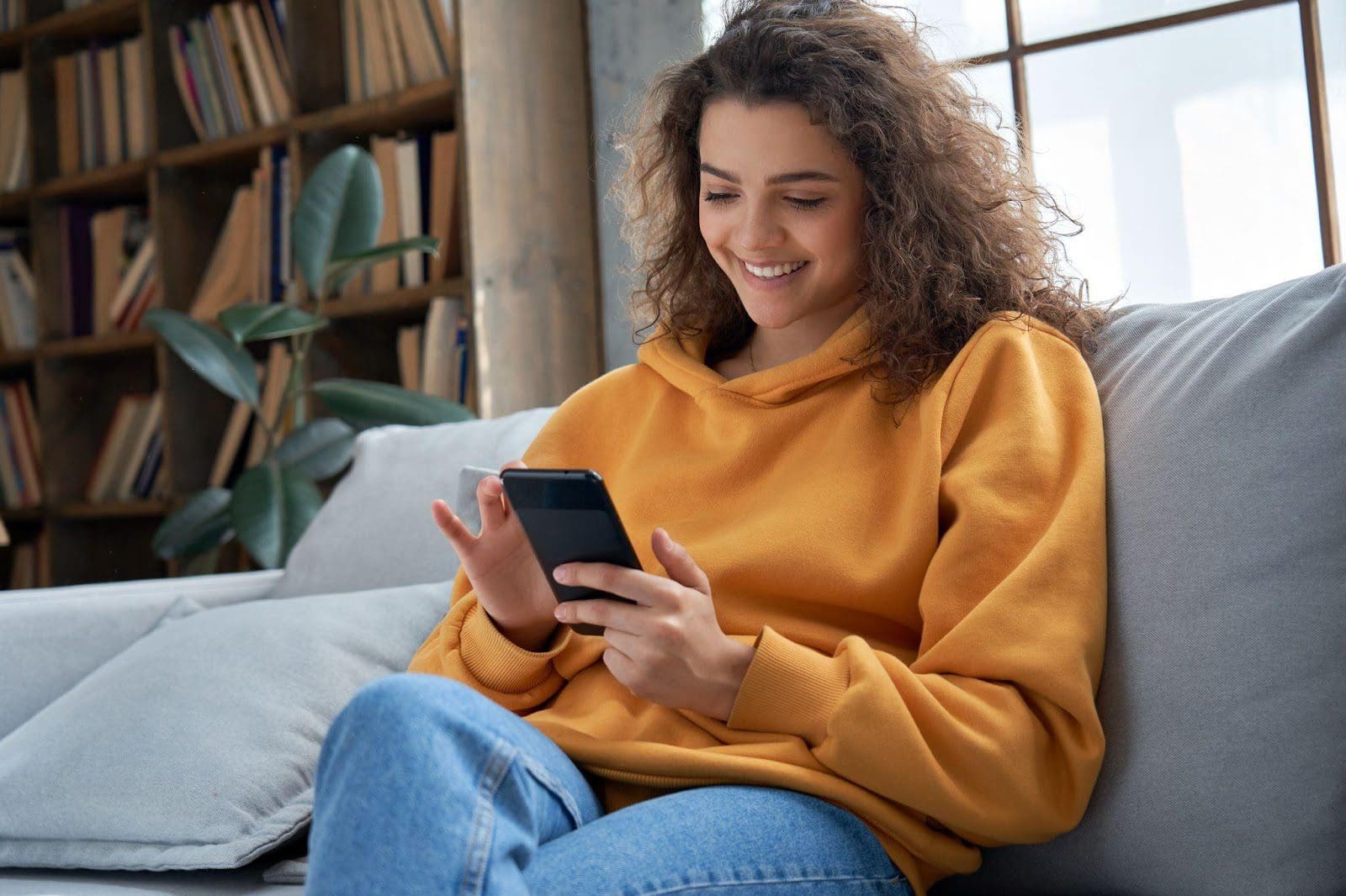 Happy young woman sitting on sofa checking her phone.