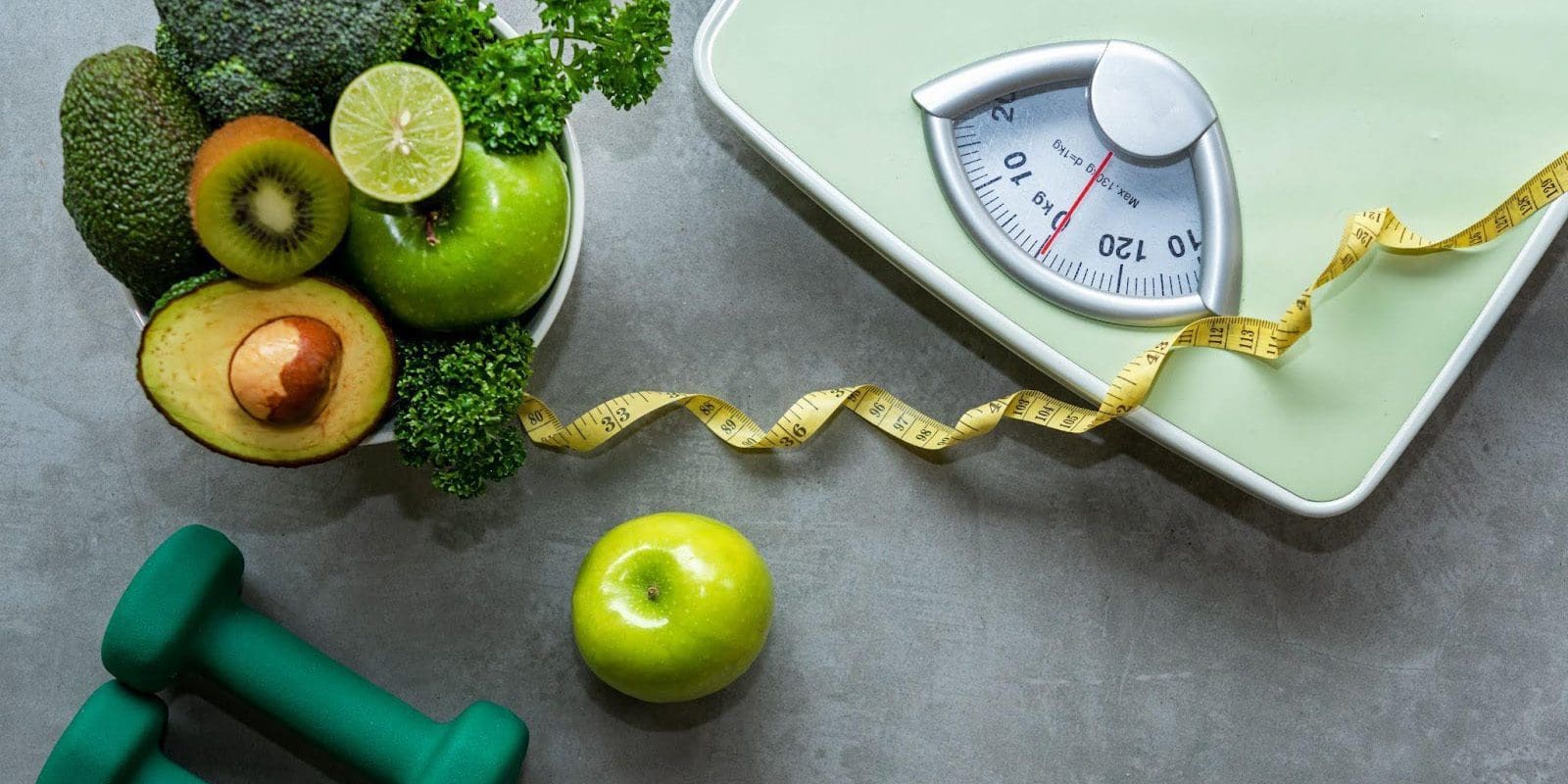 A scale, measuring tape, bowl of fruit and vegetables and hand weights.