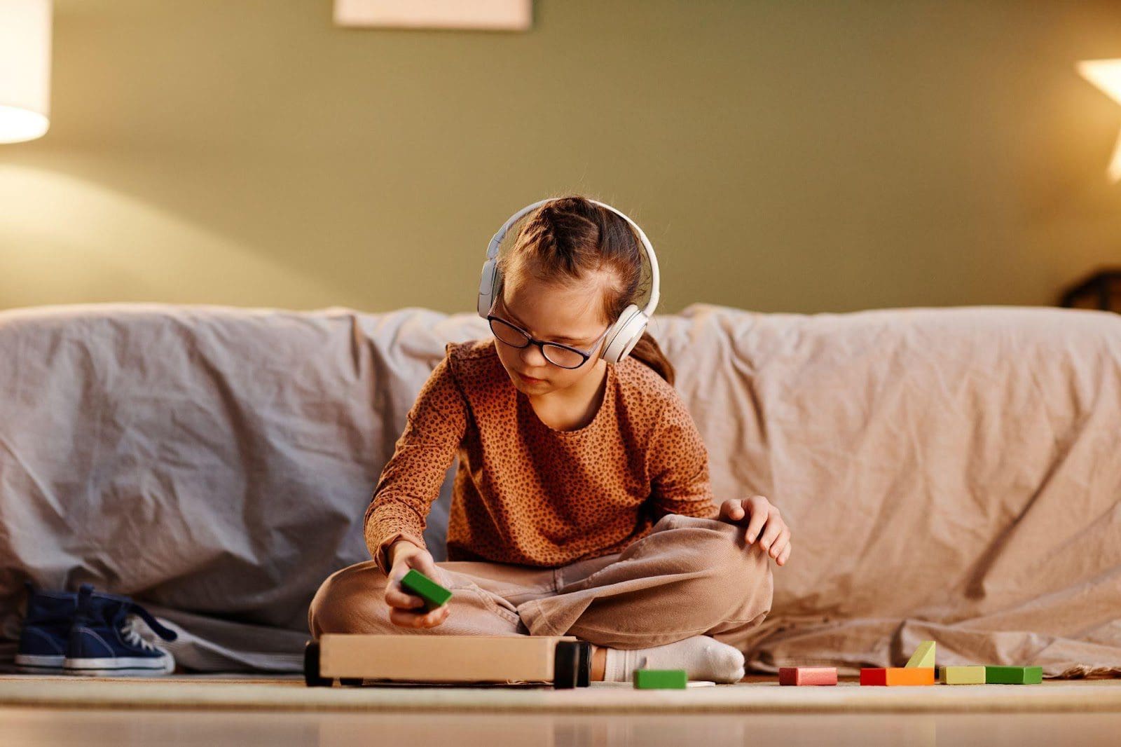 Young girl playing with blocks at home and wearing noise-canceling headphones.