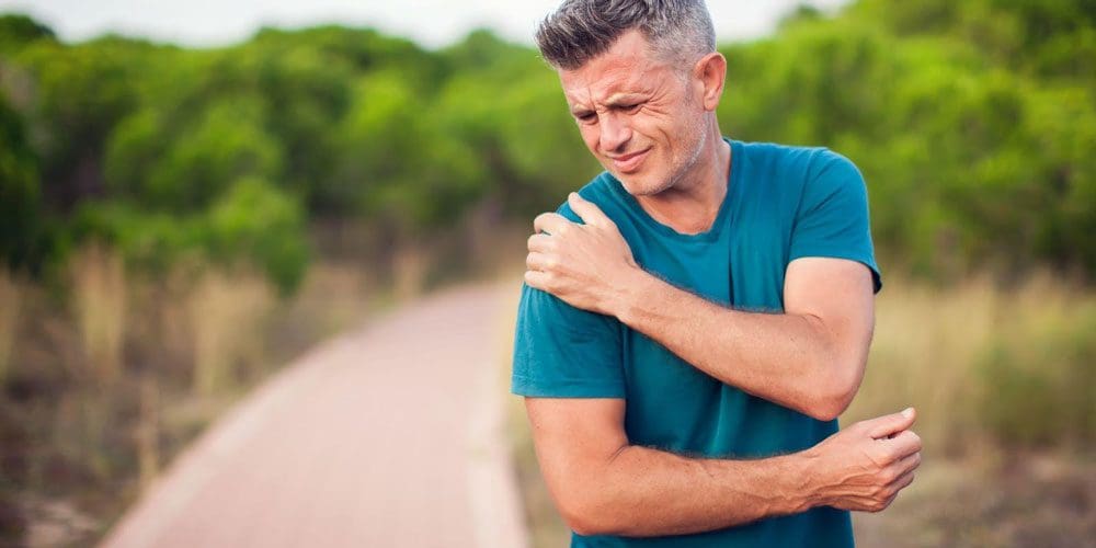Man on an outdoor trail experiencing shoulder pain.