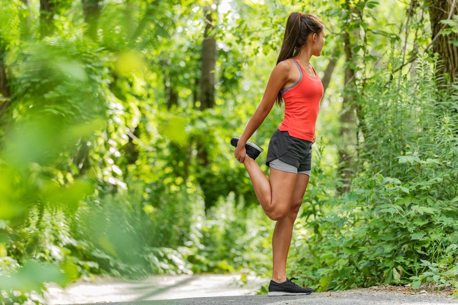 Woman stretching her thigh on a forested path.