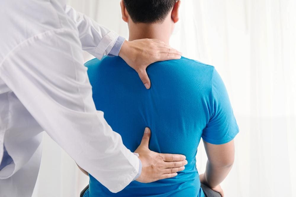 Chiropractor assessing a young male patient's back.
